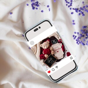 K&ouml;nnte beinhalten: Ein Smartphone-Bildschirm zeigt ein Foto eines Teddyb&auml;ren, der einen roten Rosenstrau&szlig; h&auml;lt, einen Baby-Strampler mit dem Text "Unser kleiner Valentinstag" und ein schwarzes Schild mit der Aufschrift "Baby Smith, Unser kleiner Valentinstag, 2023". Das Foto ist mit einem wei&szlig;en Rahmen versehen und hat ein rotes Herz, ein Kommentarsymbol und ein Freigabesymbol.