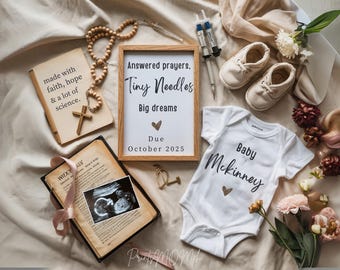 May include: A white onesie with the text "Baby Mckinney" in black script. A wooden sign with the text "Answered prayers. Tiny Needles Big dreams Due October 2025" is in the background.
