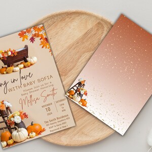 May include: A baby shower invitation with a fall theme. The invitation features a wooden cradle with pumpkins and fall leaves. The text on the invitation reads "Falling in love with Baby Sofia".