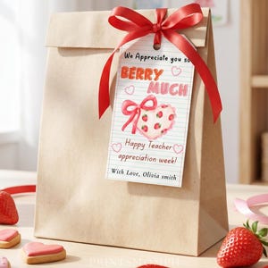 Könnte beinhalten: Eine braune Papiertüte mit rotem Band und Anhänger mit der Aufschrift "We Appreciate you so BERRY MUCH Happy Teacher appreciation week!". Erdbeeren und herzförmige Kekse sind im Vordergrund.