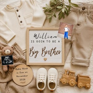 Puede incluir: Anuncio de bebé en tonos neutros. Incluye una camisa crema de punto de gofre, pantalones color beige y un letrero que dice "William is goin to be a Big Brother". Con un osito de peluche con una ecografía, un tren de madera y zapatos de bebé.