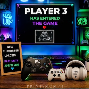 May include: A pregnancy announcement with a gaming theme. The monitor shows "PLAYER 3 HAS ENTERED THE GAME" with an ultrasound. A sign reads "NEW CHARACTER LOADING... BABY SMITH AUGUST 2026." Game controllers and headphones are also visible.