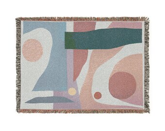 May include: Woven throw blanket with an abstract design. The blanket features a geometric pattern with shapes in shades of blue, pink, green, and white. The edges are finished with a fringe.