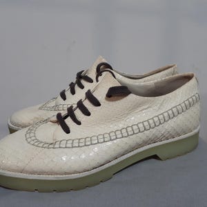 May include: White leather low-top trainers with brown laces and a textured design. The shoes have a white sole.