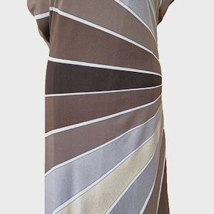 Op de afbeelding: Een bruine, beige en grijze jurk met een zonnestraalpatroon. De jurk heeft korte mouwen en een boothals. Witte strepen scheiden de kleurblokken. De jurk wordt op een mannequin getoond.