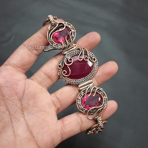 May include: A copper wire wrapped bracelet with three pink oval-shaped gemstones. The bracelet is made with a delicate wire design.