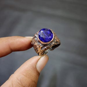 May include: A silver ring with a textured band and a large, oval-shaped blue gemstone set in a copper bezel.