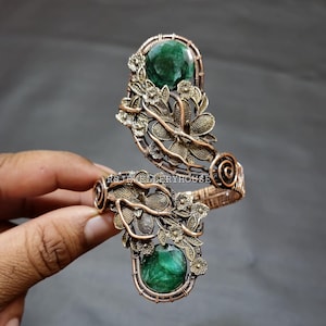 May include: A copper wire wrapped bracelet featuring two green malachite stones and a floral design.