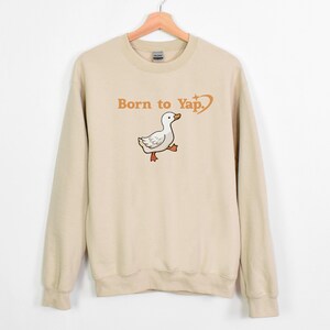 May include: A beige sweatshirt with a cartoon duck and the text "Born to Yap." printed on the front.