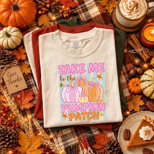 May include: A cream-colored t-shirt featuring a graphic print with the text "TAKE ME to the PUMPKIN PATCH" in pink and orange. The design includes three patterned pumpkins in pink, orange, and yellow, accented with small orange starfish.