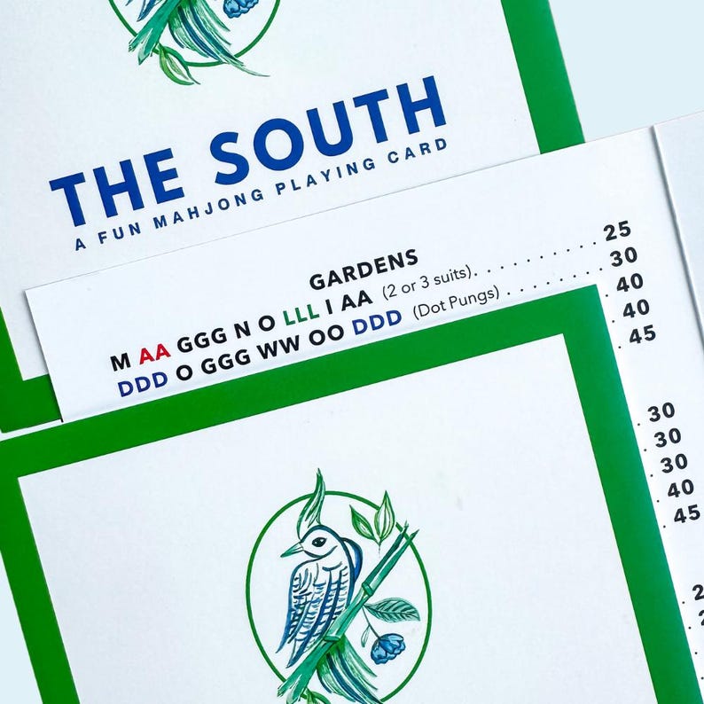 Op de afbeelding: Witte speelkaarten met groene randen en de tekst "THE SOUTH A FUN MAHJONG PLAYING CARD". De kaarten hebben een illustratie van een vogel en bamboe in een groene cirkel. De kaarten hebben ook de tekst "GARDENS".