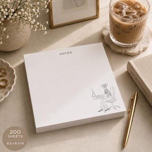 May include: A white notepad with the word "NOTES" at the top and a line drawing of a person working on a laptop. The notepad measures 8.5 x 8.5 inches and contains 200 sheets.