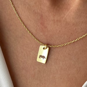 May include: A gold chain necklace with a small rectangular pendant featuring a cutout silhouette of a rhinoceros.