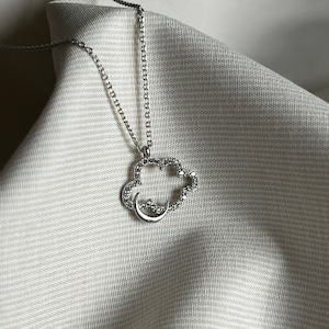 Peut inclure: Un collier en argent avec un pendentif en forme de nuage et de croissant de lune. Le pendentif est orné de petites pierres claires.