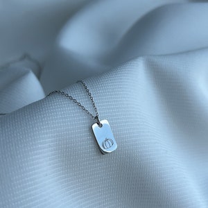 May include: A silver necklace with a small rectangular pendant featuring a simple line drawing of a pumpkin.