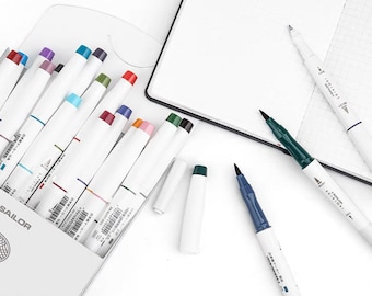 May include: A set of 16 colorful brush pens in a white plastic case with the word "SAILOR" printed on the front. The pens are arranged in a row, with the caps facing up. There are also three individual brush pens on a white surface, one green, one blue, and one white.