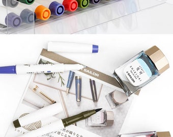 May include: A set of colorful markers in a clear plastic container, along with three bottles of ink. The ink bottles are labeled "Sailor Shikiori" and feature Japanese characters. The ink colors are blue, red, and green.