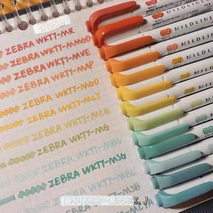 May include: A collection of Zebra Mildliner highlighters in various pastel colors. The image shows the pens with their caps and the corresponding ink swatches on a grid paper. The text on the pens and paper is visible.