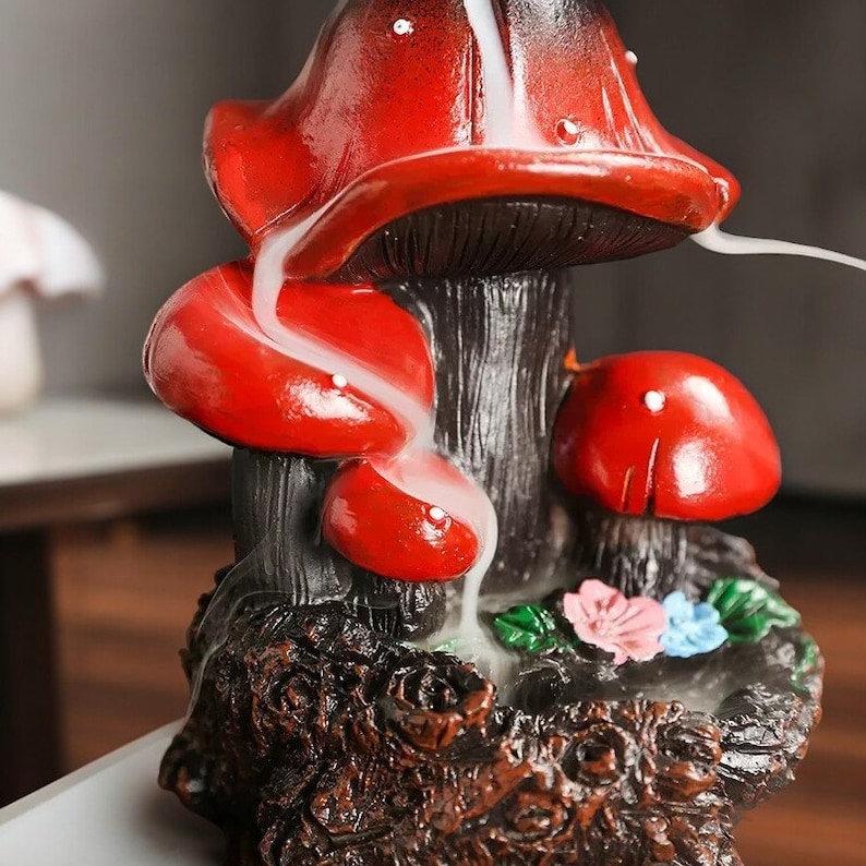 May include: A red and black ceramic incense burner shaped like mushrooms. The incense burner has three mushrooms, one large and two smaller ones. The incense burner is designed to create a smoke waterfall effect.