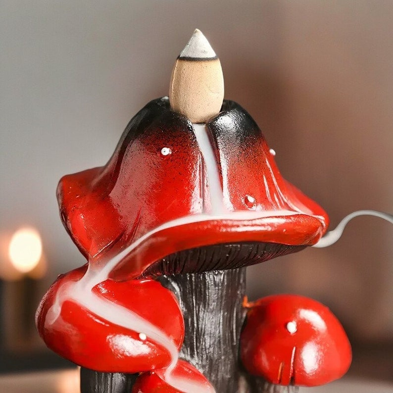 May include: Red ceramic incense burner shaped like a mushroom with a cone-shaped incense holder on top. The incense burner has a black base and white smoke is rising from the top.