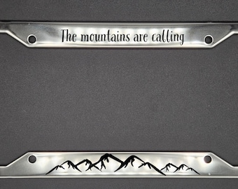 May include: A silver metal license plate frame with the text "The mountains are calling" and a silhouette of mountains at the bottom.