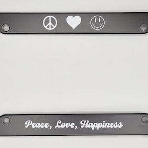 May include: Black metal license plate frame with white peace sign, heart, and smiley face symbols. The text "Peace, Love, Happiness" is printed on the bottom.