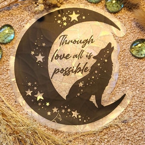 Könnte beinhalten: Ein schwarz-weißer Aufkleber mit einem Wolf, der zum Mond heult. Der Mond ist halbmondförmig und hat ein glitzerndes, irisierendes Finish. Der Aufkleber trägt den Text "Through love all is possible".