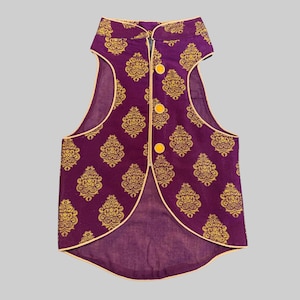 May include: A sleeveless purple vest with a gold damask pattern and three yellow buttons. The vest has a mandarin collar and is trimmed with a thin, light-colored border. The fabric has a slight sheen.