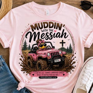 May include: A light pink t-shirt featuring a graphic of a duck wearing sunglasses and a pink headband, driving a pink off-road vehicle through mud. The text reads MUDDIN' WITH THE MESSIAH, FAITH, and I CAN DO ALL THINGS THROUGH CHRIST WHO STRENGTHENS ME. PHILIPPIANS 4:13.