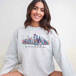 A Seattle sweatshirt with a colorful rendition of the city's skyline and the name Seattle in text. Available as a crewneck sweatshirt or hoodie.