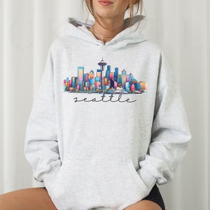 A Seattle sweatshirt with a colorful rendition of the city's skyline and the name Seattle in text. Available as a crewneck sweatshirt or hoodie.