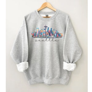 A Seattle sweatshirt with a colorful rendition of the city's skyline and the name Seattle in text. Available as a crewneck sweatshirt or hoodie.