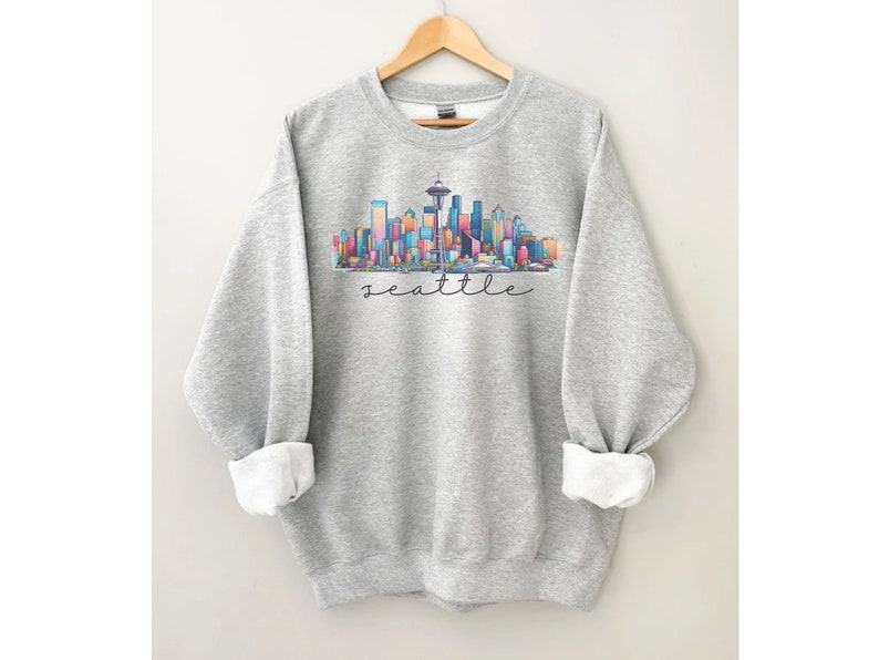A Seattle sweatshirt with a colorful rendition of the city's skyline and the name Seattle in text. Available as a crewneck sweatshirt or hoodie.