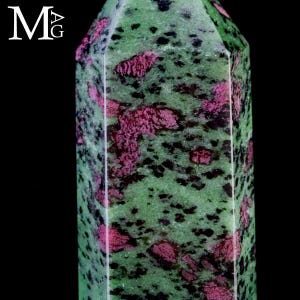 Pode incluir: Uma torre de cristal de zoisite polida com uma base verde vibrante, inclusões proeminentes de rubi cor de magenta e manchas minerais pretas espalhadas por toda a pedra. O cristal tem uma forma hexagonal facetada com arestas vivas.