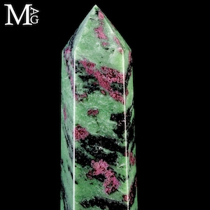Pode incluir: Uma torre de pedra polida com topo pontiagudo, apresentando um padrão manchado de verde vibrante, preto profundo e inclusões minerais rosa magenta. As letras M e G estão impressas em branco no canto superior esquerdo da imagem.
