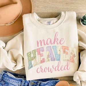 Puede incluir: Sudadera color crema con la frase "make HEAVEN crowded" en rosa y letras de patchwork. Las letras están decoradas con telas florales y estampadas. Un sombrero marrón y unos shorts vaqueros también están en la imagen.