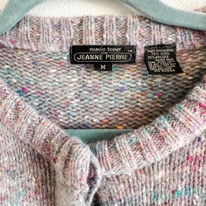 May include: A light gray knit cardigan with a multicolored speckled pattern, featuring a ribbed crew neckline and a button-front closure. The interior label reads Renee Tener for Jeanne Pierre, size M, made of 70% wool and 30% angora rabbit hair.