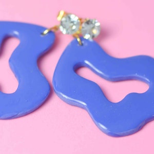 May include: A pair of blue abstract shaped earrings with clear rhinestone accents.