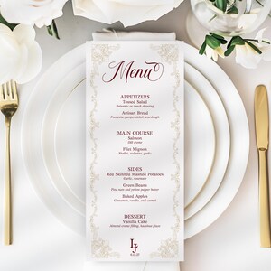 May include: A formal menu card with a decorative border and the word "Menu" in elegant script. The menu lists appetizers, main courses, sides, and dessert. Gold-coloured silverware and white plates surround the menu card, with white flowers in the background.