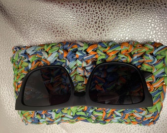 May include: Black sunglasses with a crocheted case made of blue, green, and orange yarn.