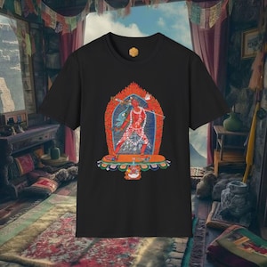 Puede incluir: Camiseta negra con un gráfico vibrante de una figura roja sosteniendo un arma, sobre un fondo azul y naranja. El diseño está enmarcado por un arco ornamentado. La camiseta tiene cuello redondo y un pequeño emblema dorado cerca del cuello. El tema es espiritual o cultural.