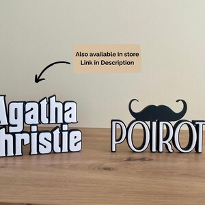 Pu&ograve; includere: Due insegne con nomi 3D in bianco e nero, una con la scritta "Agatha Christie" e l'altra "Poirot" con un paio di baffi. Le insegne sono su una superficie di legno. &Egrave; visibile anche il testo "Also available in store Link in Description".