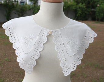 May include: White cotton lace collar with scalloped edges and delicate floral embroidery. The collar has a pearl button fastening.