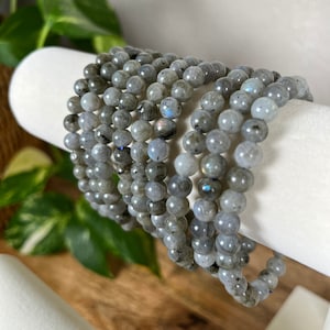 May include: A stack of grey labradorite gemstone bracelets. Each bracelet is made of round beads and has a subtle iridescent sheen.