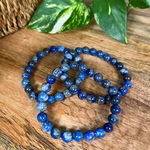 May include: Three blue lapis lazuli beaded bracelets stacked on a wooden surface.