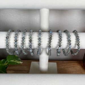 May include: A set of eight grey gemstone bracelets displayed on a white jewellery stand. The bracelets are made of small, round beads.