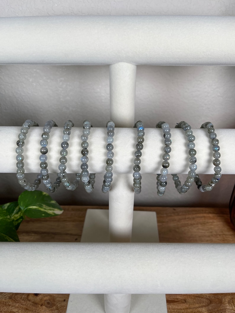 May include: A set of eight grey gemstone bracelets displayed on a white jewellery stand. The bracelets are made of small, round beads.