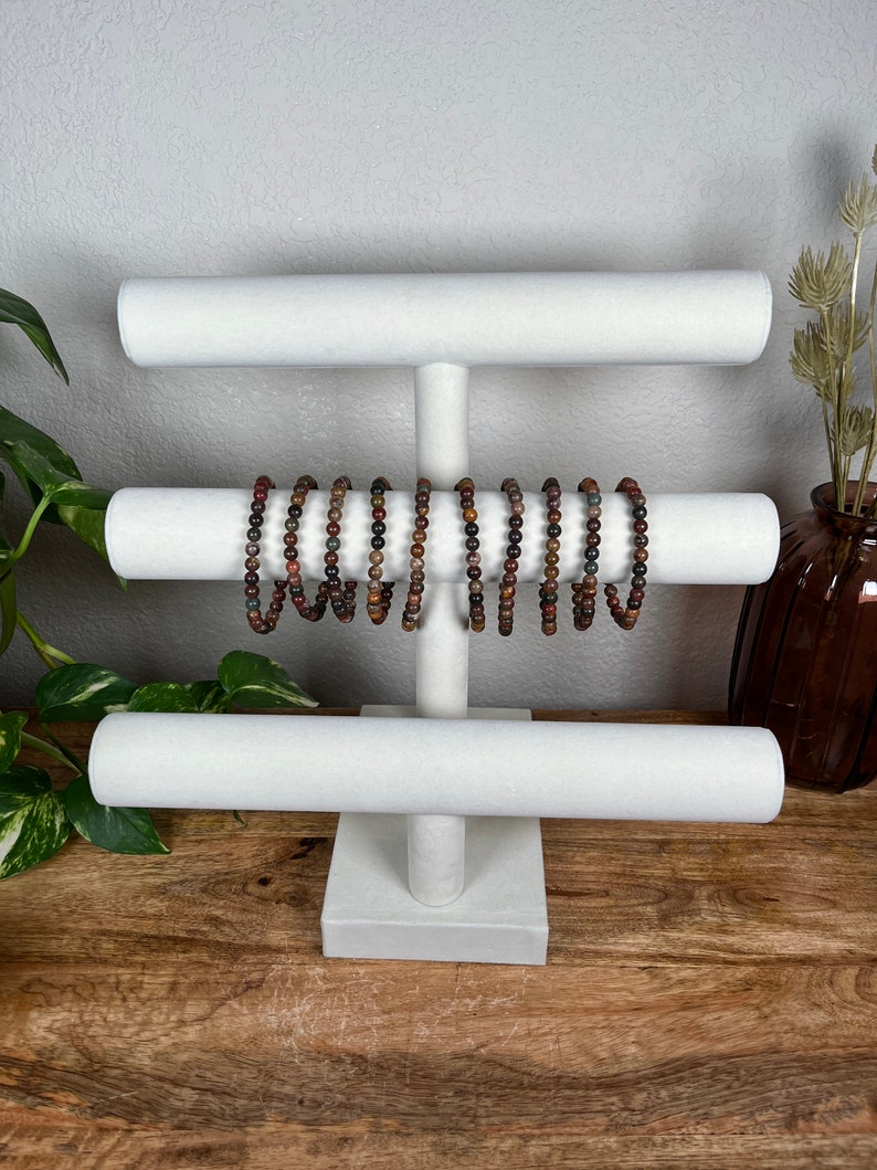 May include: White jewelry display stand with three tiers. The stand is made of wood and has a white fabric covering. There are several brown and red beaded bracelets on the stand.
