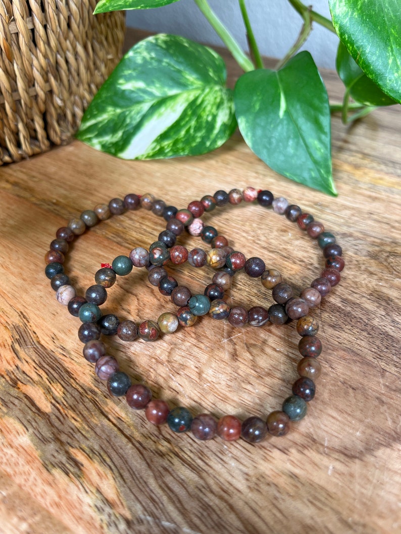 May include: Three layered bracelets made of brown, red, and green jasper beads.