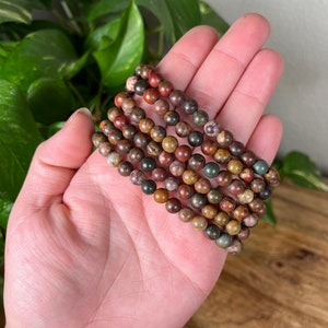May include: A stack of six bracelets made with brown, green, and red jasper beads.